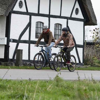 Cykellister cykler forbi gammel bindingsværkhus på Herregårdsruten